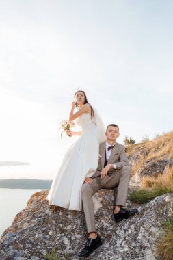Pretty bride and stylish groom. Beautifull wedding couple embracing near the shore of a mountain river with stones. Wedding at Bakota.