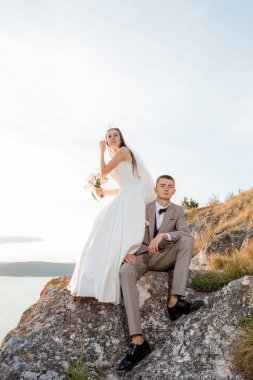 Pretty bride and stylish groom. Beautifull wedding couple embracing near the shore of a mountain river with stones. Wedding at Bakota.