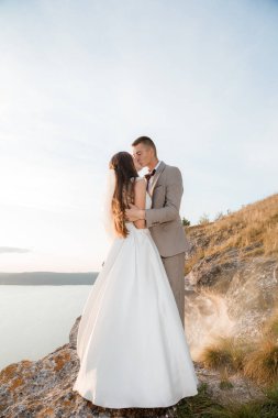 Pretty bride and stylish groom. Beautifull wedding couple embracing near the shore of a mountain river with stones. Wedding at Bakota.