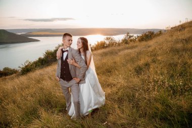 Pretty bride and stylish groom. Beautifull wedding couple embracing near the shore of a mountain river with stones. Wedding at Bakota.
