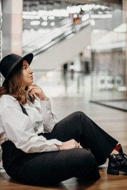 Pantolon askısı ve beyaz gömlek giyen sarışın bir mankenin portresi..