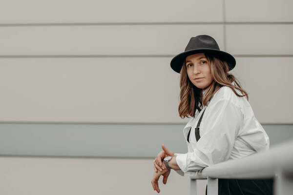 Elegant fashionable woman wearing white shirt, black hat. Confident girl posing black suit and hat. Business girl in suit.