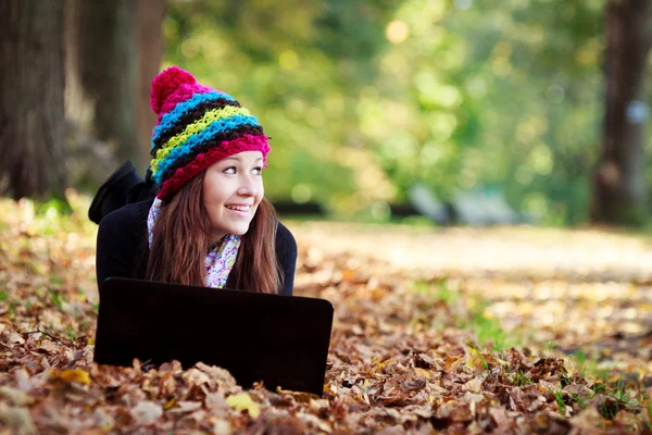 Hermosa adolescente que trabaja en el ordenador portátil en el parque durante el otoño Imagen de stock
