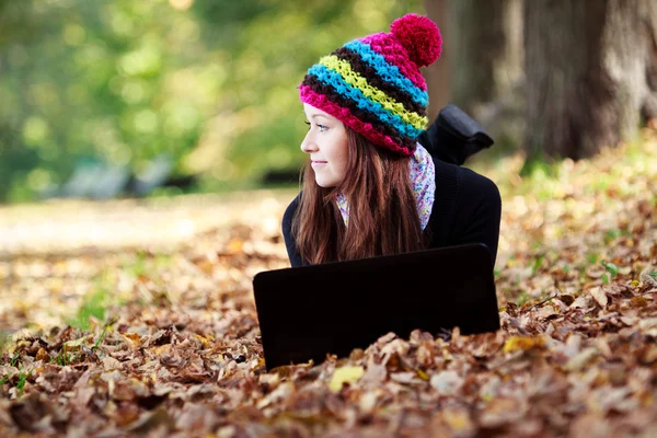 Bella ragazza con computer portatile nel parco autunnale. Giovani europei Immagine Stock
