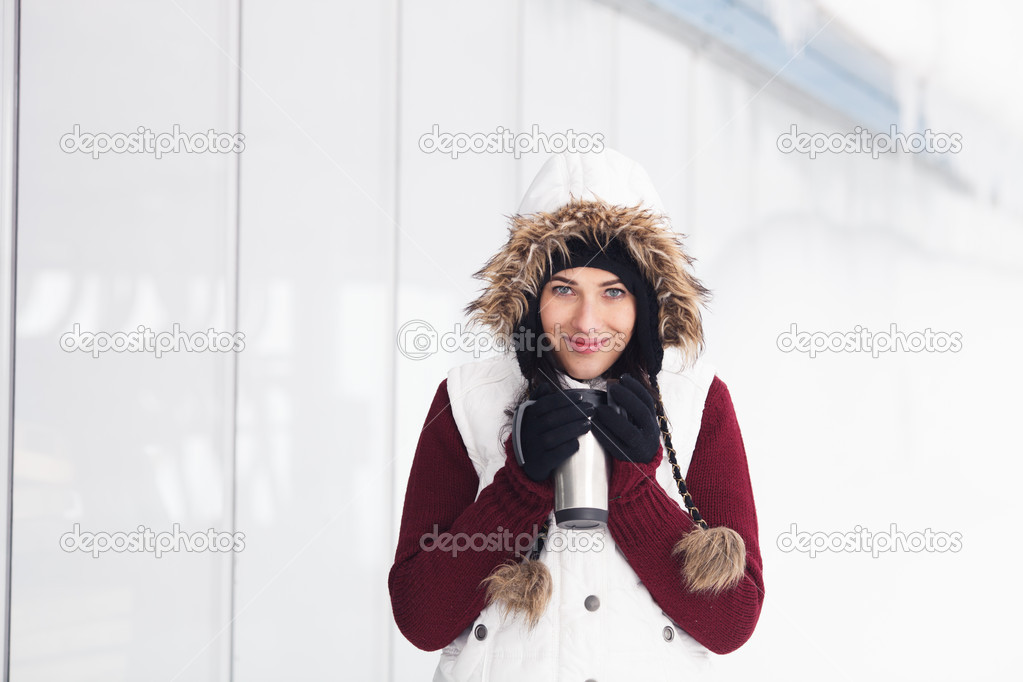 Beautiful smiling girl holding thermos in snowy winter outdoors
