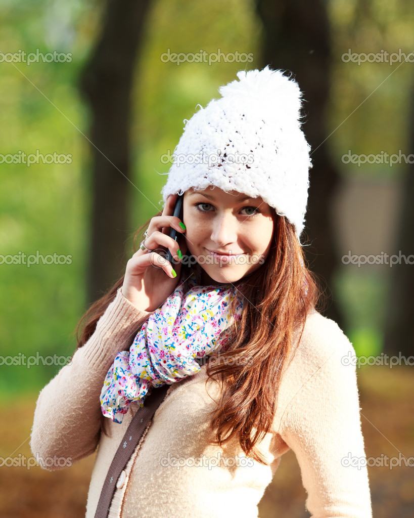 Pretty young woman talking on new cell phone in autumn park