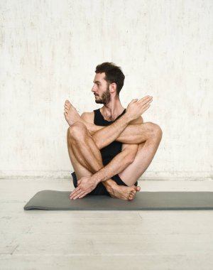 Genç bir adam yoga yapıyor. Yoga koçu hafif arka planda.