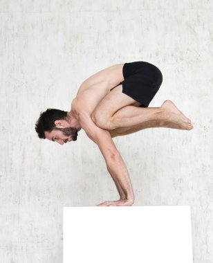 Genç bir adam yoga yapıyor. Yoga koçu hafif arka planda.