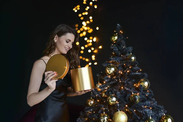 クリスマスツリーを背景に美しい若い女性。新年の贈り物だ。黒の背景魔法の贈り物 — ストック写真