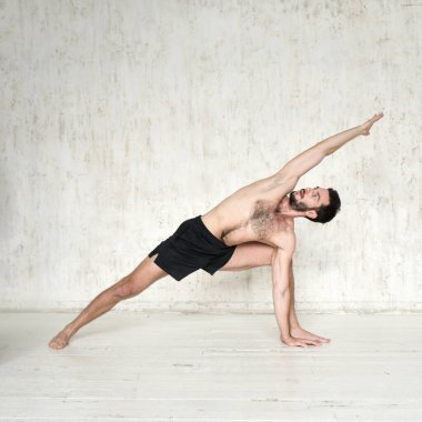 Genç bir adam yoga yapıyor. Yoga koçu hafif arka planda.