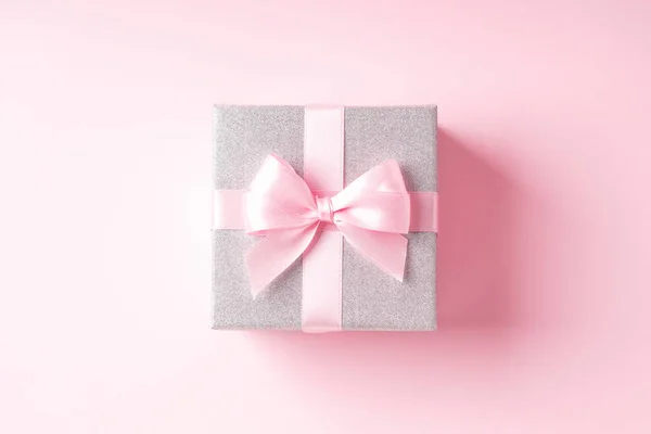 Pembe arka planda pembe kurdeleli gümüş parıltılı hediye kutusu. Noel, Sevgililer Günü ya da doğum günü konsepti. Mesaj için yer. Üst görünüm.