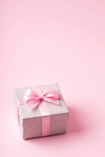 Zilveren glitter geschenkdoos met roze lint strikje op roze achtergrond. Kerstmis, Valentijnsdag of verjaardag concept. — Stockfoto