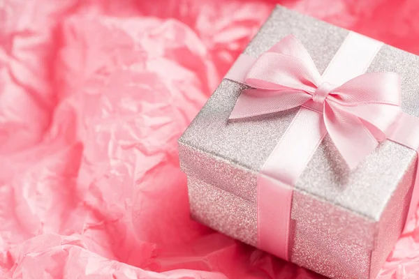 Stříbrný třpyt dárková krabice s růžovou stuhou luk na růžovém pozadí. Vánoce, Valentýn nebo narozeninový koncept. — Stock fotografie