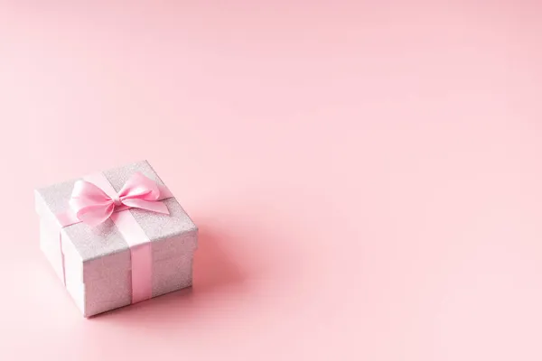 Silber glitzernde Geschenkschachtel mit rosa Schleife auf rosa Hintergrund. Weihnachten, Valentinstag oder Geburtstag Konzept. — Stockfoto