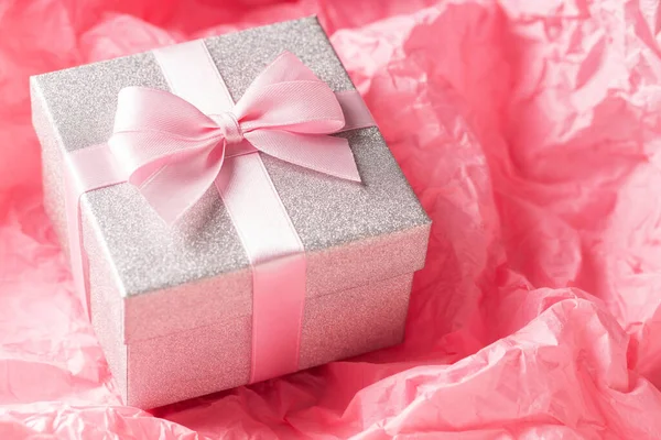 Zilveren glitter geschenkdoos met roze lint strikje op roze achtergrond. Kerstmis, Valentijnsdag of verjaardag concept. — Stockfoto