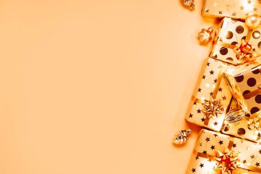 Altın fiyonklu hediye kutuları, Noel ağacı oyuncakları ve bej arka planda ışıklar..