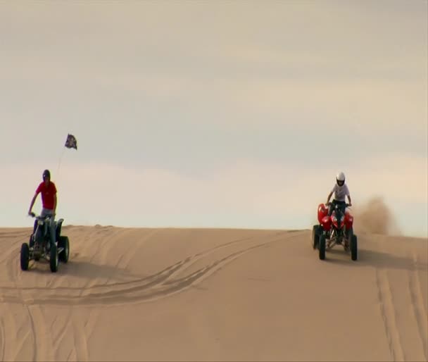 ATV riders come over sand dune and past camera — Stock Video