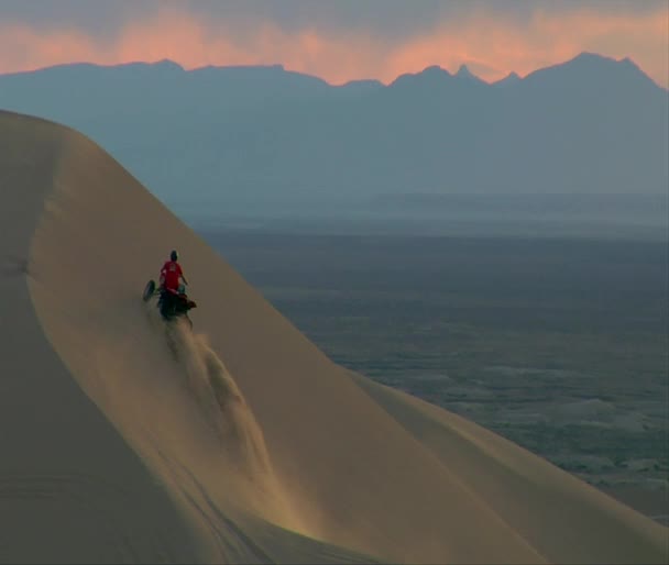 ATV ryttare skalor branta sanddyn med berg och avstånd — Stockvideo
