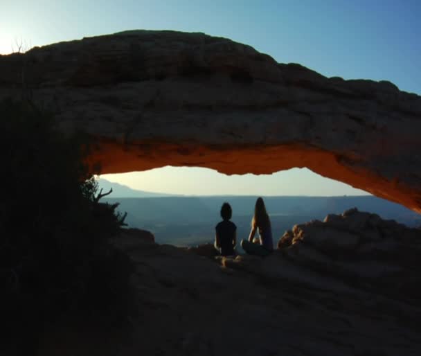 Women sit under Mesa arch — Stock Video