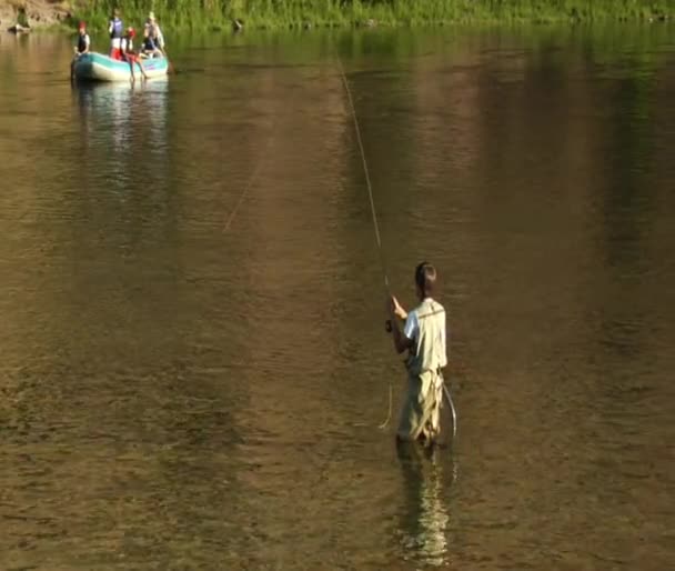 Jonge man flyfishing in slow motion met drijfnetten boot op achtergrond — Stockvideo