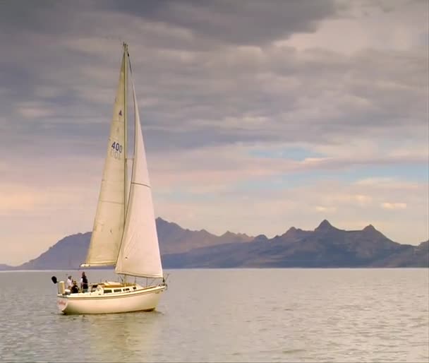 Un velero se desliza sobre aguas tranquilas cerca de las montañas — Vídeos de Stock