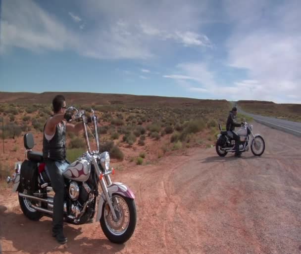 Мотоциклисты отдыхают на обочине пустынной дороги — стоковое видео