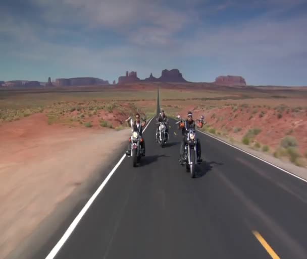 Three bikers on a desert highway, mesas behind — Stock Video