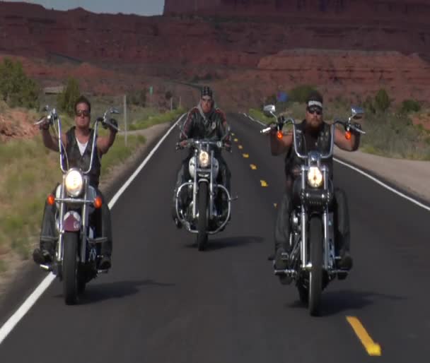 Three bikers on a desert highway, mesas behind — Stock Video