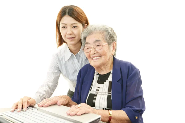 Yaşlı bir bayan bir bilgisayar kullanmak yardımcı öğretmen — Stok fotoğraf