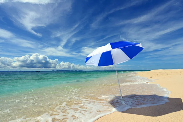 Beach umbrella on a sunny beach with the blue sea in the background. — Stock Photo, Image