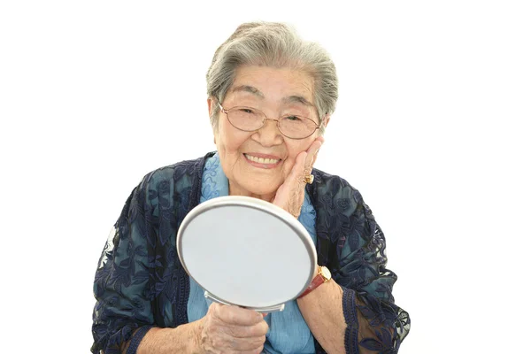 Velha mulher olhando para si mesma em um espelho de mão — Fotografia de Stock
