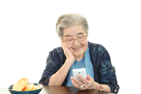 Gammel kvinne som smiler med mobiltelefon – stockfoto