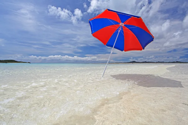 Beach umbrella on a sunny beach with the blue sea in the background. — Stock Photo, Image