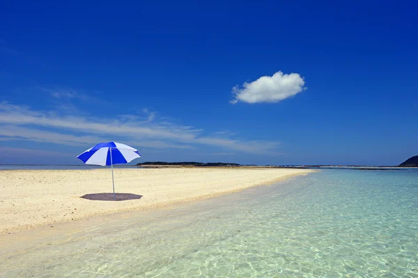 Parasoll på en solig strand med blå havet i bakgrunden. — Stockfoto