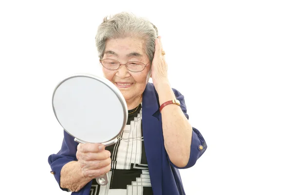 Oude vrouw kijken naar zichzelf in een hand spiegel — Stockfoto