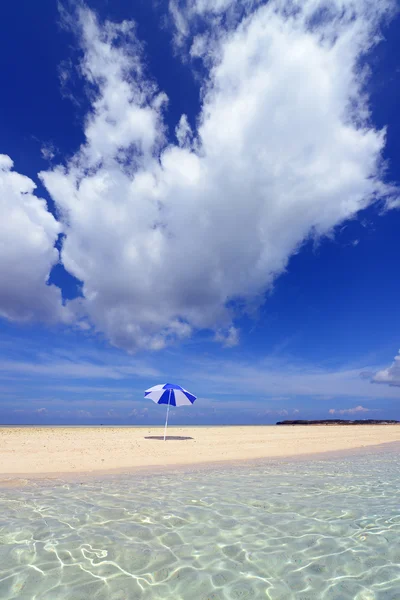 Strandparasol op een zonnig strand met de blauwe zee op de achtergrond. — Stockfoto