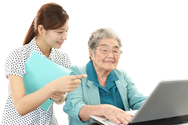 Jonge vrouw helpt een oudere dame die een computer gebruiken — Stockfoto