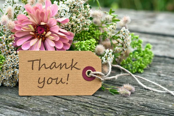 Thank you written on a gift tag attached to a bouquet of flowers, on a wooden table