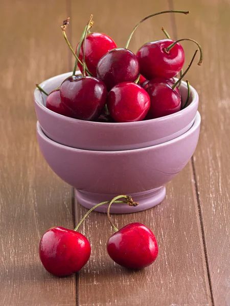 Körsbär i en skål på en träbricka — Stockfoto