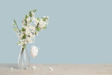Mutlu Paskalyalar. Bahar bayramında yumurta, beyaz çiçekli meyve dalları küçük kristal vazoda narin mavi arka planda. Kopya alanı olan taze çiçek arkaplanı