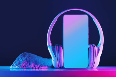 Kablosuz kulaklıklı, neon ışıklı siber punk fütüristik arka planlı akıllı telefon modeli. Uzayı kopyala Ses teknolojisi uygulamaları, müzik podcast kitapları