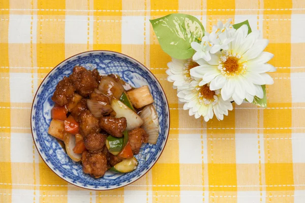 Sweet and sour pork and white artificial flowers — Stock Photo, Image