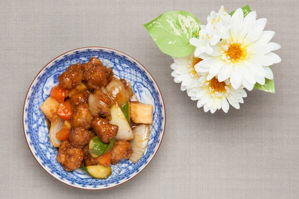 Sweet and sour pork and white artificial flowers — Stock Photo, Image