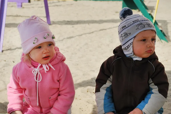 Um menino e uma menina sentados em uma caixa de areia — Fotografia de Stock