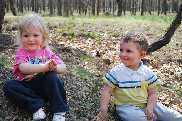 Pojke och flicka sitter i en skog — Stockfoto