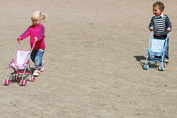 Kleine jongen en meisje spelen met kinderwagens. — Stockfoto