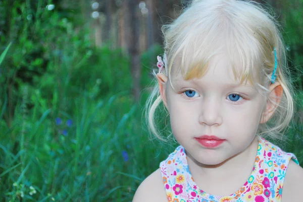 In forest, a little serious girl is sitting in the tall grass — Stock Photo, Image