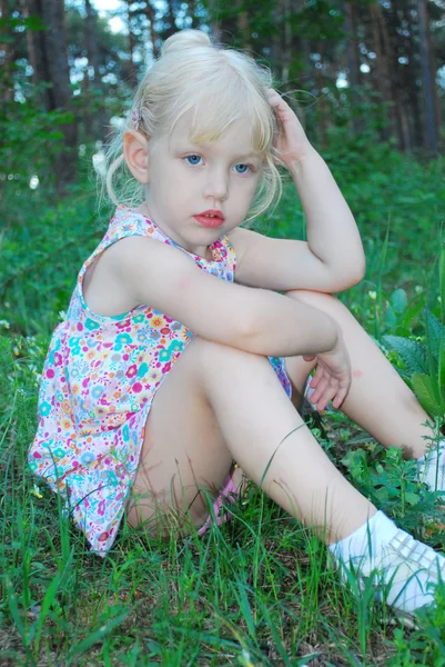 In forest, a little serious girl is sitting in the tall grass — Stock Photo, Image