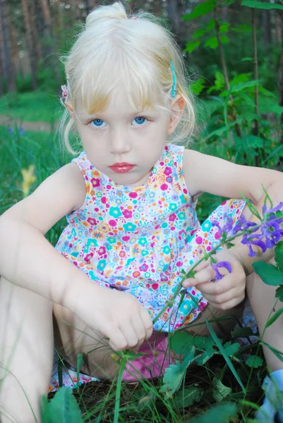 In forest, a little serious girl is sitting in the tall grass — Stock Photo, Image