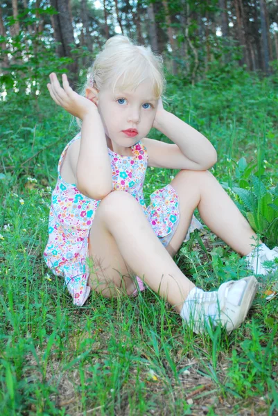 In forest, a little serious girl is sitting in the tall grass — Stock Photo, Image